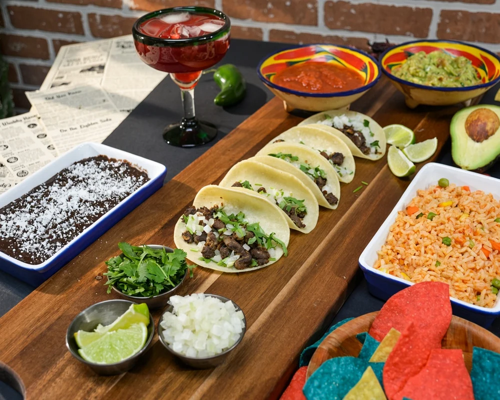 Hot tacos with cilantro and onion on a wooden board with Mexican rice, black beans, salsa and guacamole from Tres Marias in Calgary, AB